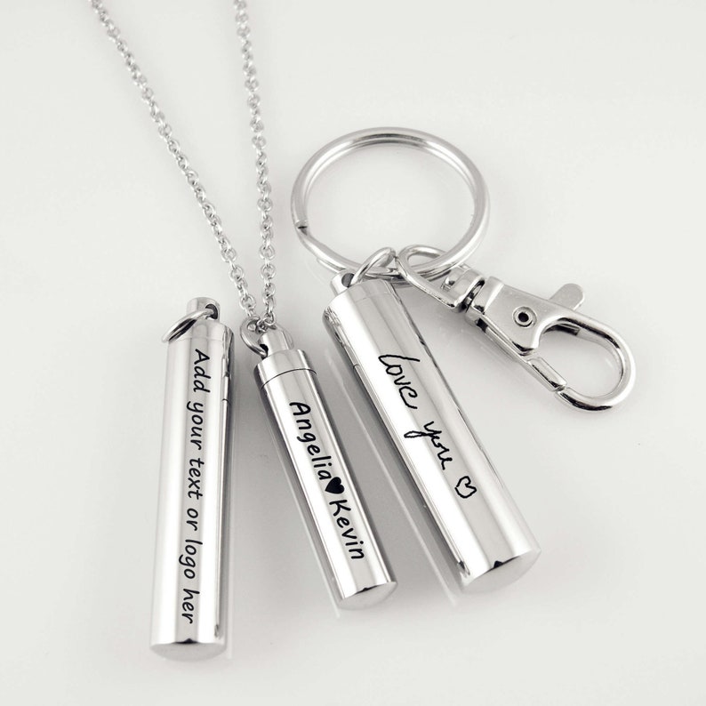 May include: Three silver metal cremation urns with engraved text. The urns are attached to chains and a key ring. The text on the urns reads "Add your text or logo here", "Love you", and "Angelia Kevin".