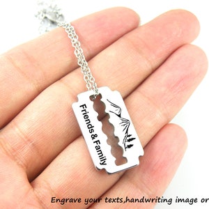 Könnte beinhalten: Silberne Halskette mit einem Rasiermesser-Anhänger, der mit "Friends & Family" und einer Bergszene graviert ist.