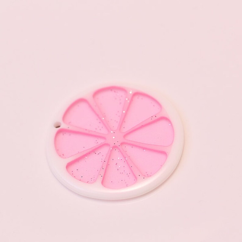 May include: A pink and white plastic lemon slice charm with glitter.