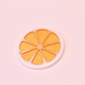 May include: A white and orange plastic charm shaped like a slice of orange with gold glitter inside.