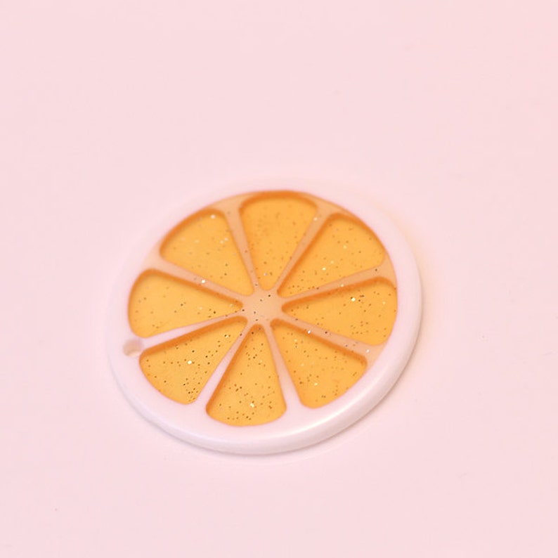 May include: A white and orange plastic charm shaped like a slice of orange with gold glitter inside.