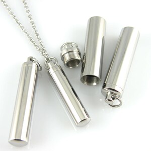 May include: A silver necklace with a cylindrical pendant that can be opened and closed. The pendant is attached to a silver chain.