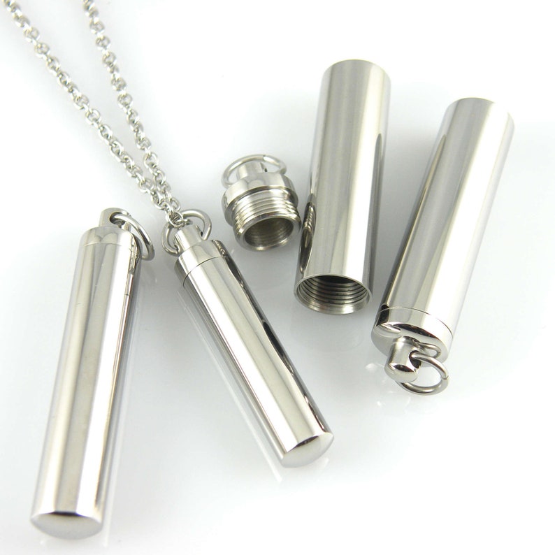 May include: A silver necklace with a cylindrical pendant that can be opened and closed. The pendant is attached to a silver chain.