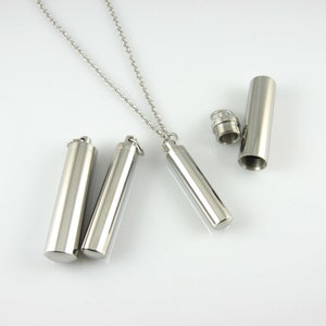 May include: Three silver cylindrical pendants with a silver chain. Two pendants are closed and one is open, revealing an empty interior.