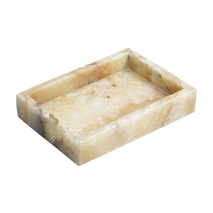 Puede incluir: Una bandeja rectangular hecha de alabastro marrón claro y blanco. La bandeja tiene una superficie lisa y pulida y un borde ligeramente elevado.