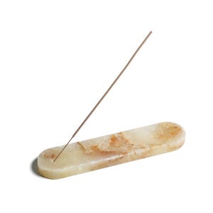 May include: A light green and brown marble incense holder with a single incense stick resting on top.
