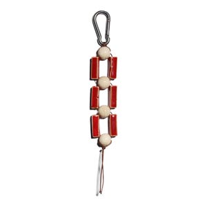 May include: A decorative keychain featuring a silver carabiner clip, cream-colored beads, and red rectangular ceramic tiles. The keychain has a brown string tassel at the bottom. The design is symmetrical and modern.