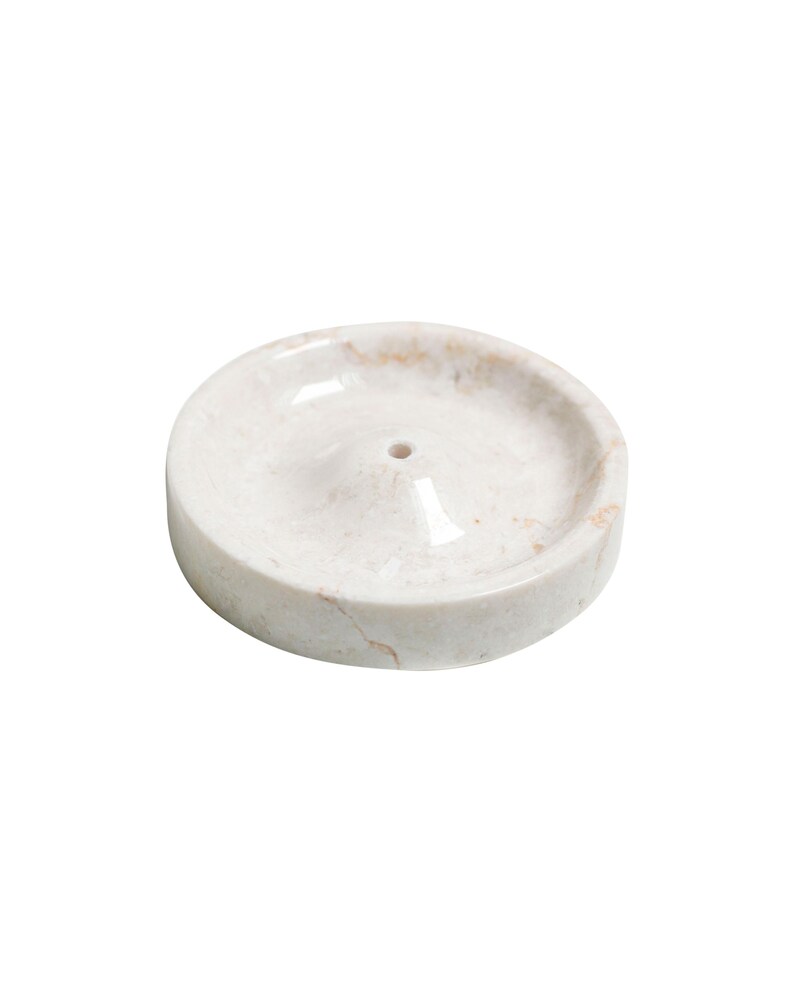 May include: White marble incense holder with a small hole in the center. The holder has a slightly raised edge and a smooth, polished surface.