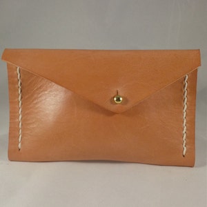 May include: A light brown leather envelope clutch with a gold button closure and white stitching.