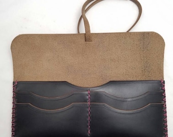 Puede incluir: Una cartera de cuero negro con costuras rosas y una solapa de cuero marrón. La cartera tiene múltiples ranuras para tarjetas y un cierre de solapa.