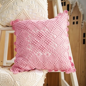 May include: Three crocheted pillow covers in white and pink. The pillows are stacked on a white wooden step stool. The pillows have a delicate, lacy design.