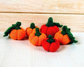 May include: A group of six crocheted pumpkins in various shades of orange and red. The pumpkins have green stems and leaves.