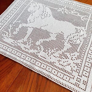 May include: A white, crocheted rectangular doily featuring a horse design in the center. The doily has a detailed, openwork pattern with a decorative border. The horse is depicted in a running pose, adding a touch of elegance to the handmade piece.