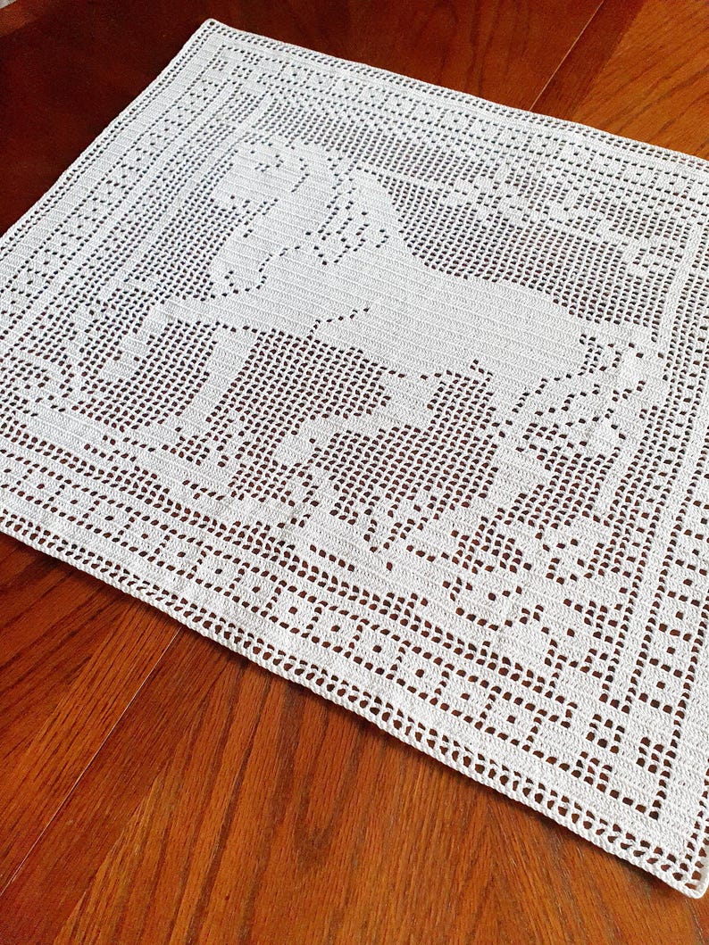 May include: A white, crocheted rectangular doily featuring a horse design in the center. The doily has a detailed, openwork pattern with a decorative border. The horse is depicted in a running pose, adding a touch of elegance to the handmade piece.