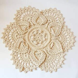 May include: A large, cream-colored crocheted doily with a delicate floral pattern. The doily is made with a thick, textured yarn and has a scalloped edge.
