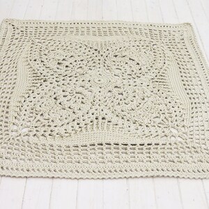 May include: A large, square, crocheted throw blanket in a light beige color. The blanket has a delicate, intricate pattern with a central square motif.