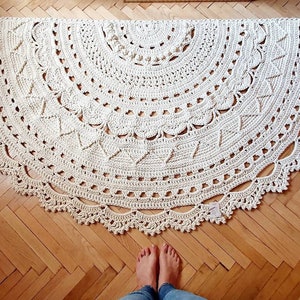 May include: A large, cream-colored crocheted rug with a circular design. The rug has a delicate, lacy border and intricate patterns throughout.