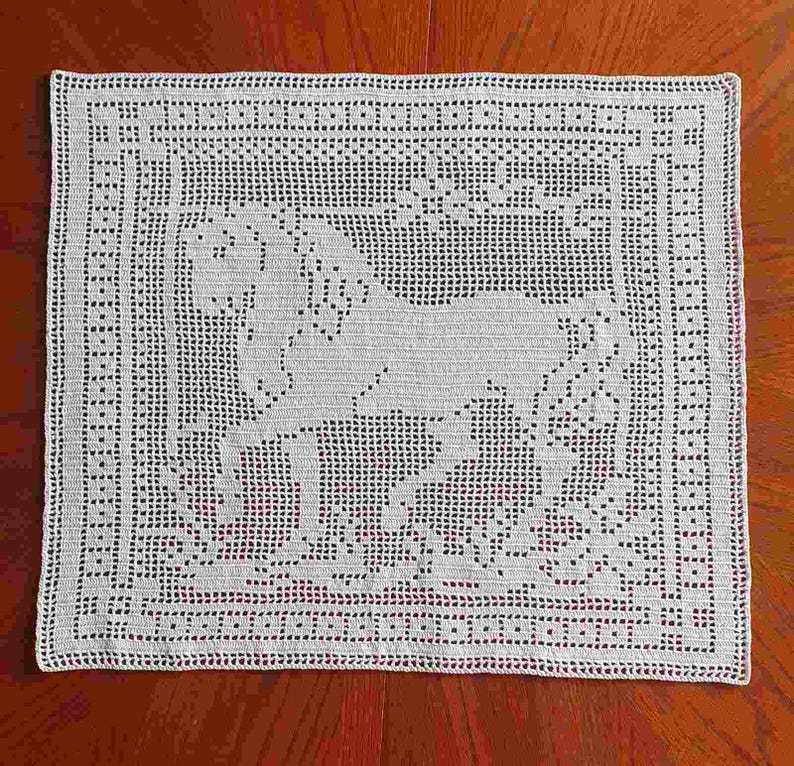 May include: A white, square, crocheted doily featuring a horse design in the center. The horse is surrounded by floral and geometric patterns. The doily is made of a fine, open-weave material.