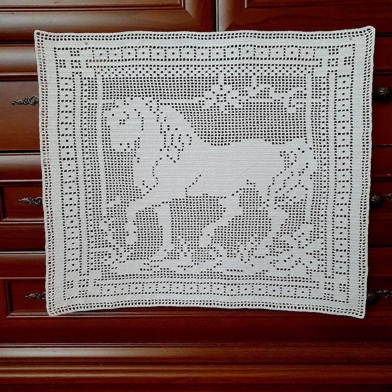 May include: A square, off-white crocheted doily featuring a detailed horse design in the center. The doily has a decorative border with a repeating pattern of small holes. The handmade textile is placed on a dark wooden surface.