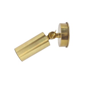 May include: A brass wall-mounted spotlight with a cylindrical shade and a round base. The spotlight is adjustable and can be tilted up or down.
