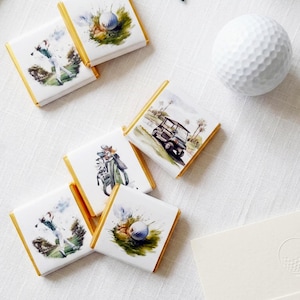 May include: A top-down view shows golf-themed party favours and accessories. Square chocolates with gold edges feature golf course illustrations. A white golf ball, green tees, and a menu card with the text "Happy 50th, John!" are also present.