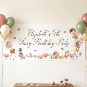 May include: A fairy-themed birthday party banner with the text "Elizabeth's 4th Fairy Birthday Party." The banner features illustrations of fairies, mushrooms, and flowers. Balloons in pink, green, and gold are arranged on either side of the banner.