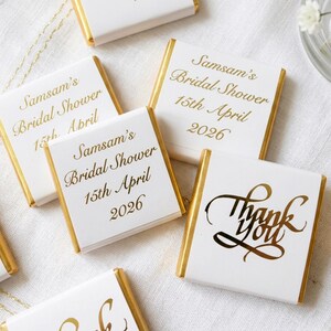 May include: White chocolate bars with gold foil edges and gold lettering. The bars are printed with "Samsam's Bridal Shower 15th April 2026" and "Thank You" in elegant script. A bridal shower theme.