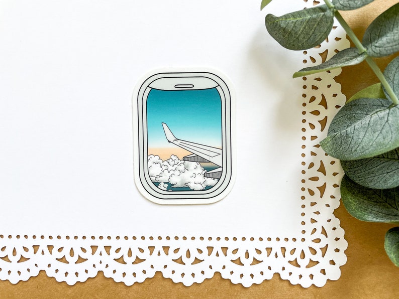 May include: A sticker of an airplane wing seen through an airplane window. The window is outlined in white and the sticker is on a white background.