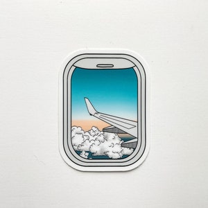 May include: A sticker of an airplane window view with a wing and clouds in the distance. The sky is blue with a sunset in the background.