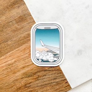 May include: A sticker of an airplane wing seen through an airplane window. The window is outlined in white and the sticker is on a white background.