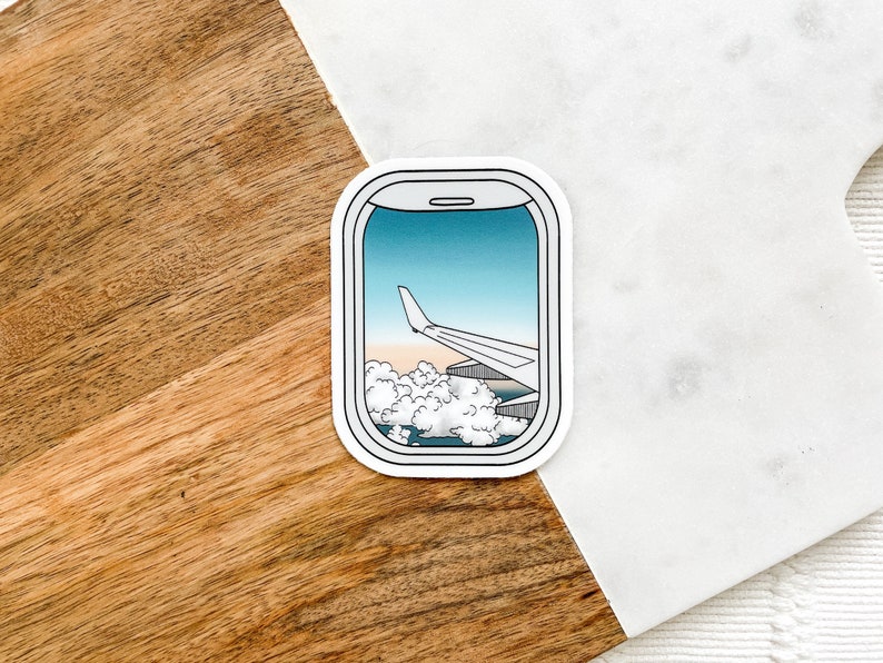 May include: A sticker of an airplane wing seen through an airplane window. The window is outlined in white and the sticker is on a white background.
