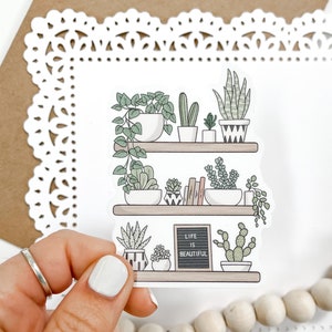 May include: A white sticker with a hand-drawn illustration of a shelf with potted plants and the text "Life is Beautiful" on a chalkboard.