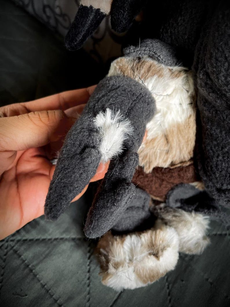 Op de afbeelding: Close-up van een pluche speelgoed met grijs haar en bruine accenten. Het speelgoed heeft een lange, puntige staart en een harige, witte vlek op zijn rug.