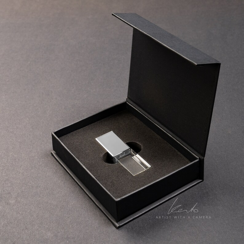 May include: A silver and clear crystal USB drive in a black gift box. The box is open and the drive is sitting in the center of the box.