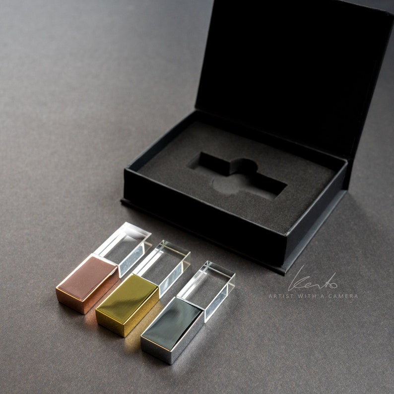 May include: Four crystal USB drives in a black box. The drives are in different colors: rose gold, gold, silver, and clear. The box has a black interior and a black exterior with the text "kento ARTIST WITH A CAMERA" printed on the bottom.
