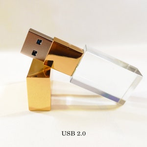 May include: A gold and clear crystal USB flash drive with a USB 2.0 connector. The drive is designed to look like a small rectangular prism.
