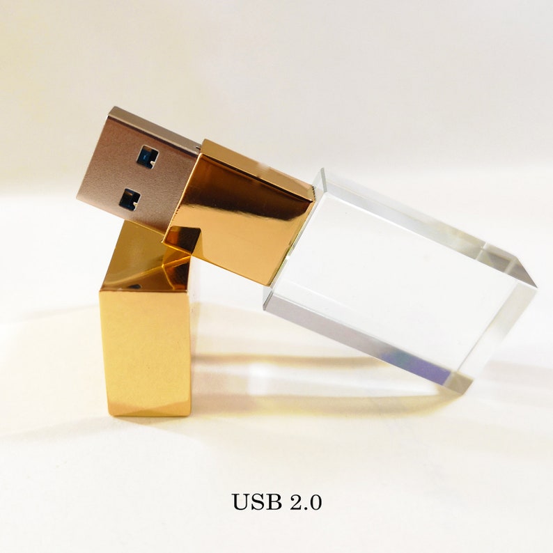 May include: A gold and clear crystal USB flash drive with a USB 2.0 connector. The drive is designed to look like a small rectangular prism.