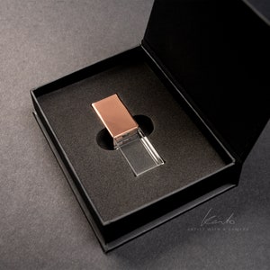 May include: A clear crystal USB drive with a rose gold top in a black velvet box. The box is open and the drive is sitting inside.