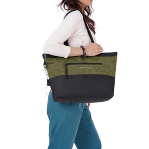 Close up view of brown haired model facing the side. She is wearing a white top and blue pants. On her shoulder she carries Sherpani's Anti-Theft tote the Cali AT in Loden.