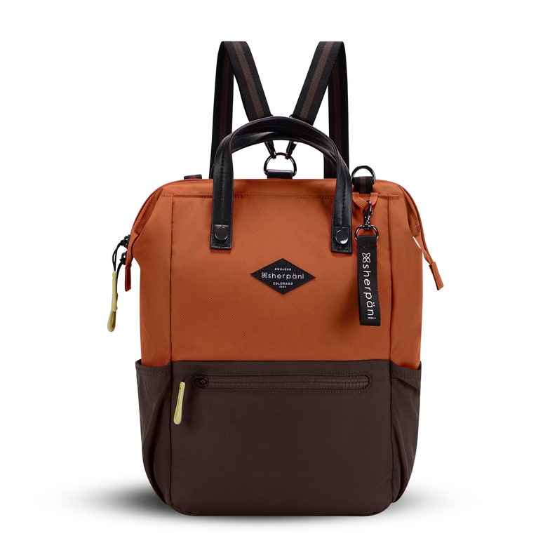 Flat front view of Sherpani three-in-one bag, the Dispatch in Clay. The bag is two-toned: the top is orange and the bottom is brown. There is an external zipper pocket on the front panel. Easy-pull zippers are accented in lime green.