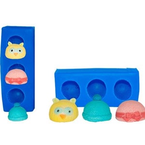 May include: Blue silicone molds for making small cake pops or other treats. The molds feature three different designs: an owl, a blue hat, and a pink hat with a bow.