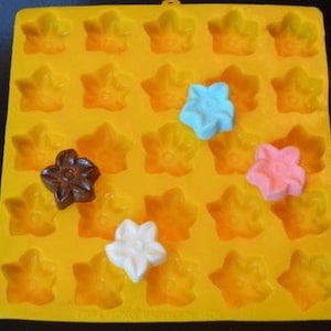 Könnte beinhalten: Eine gelbe Silikonform mit sternförmigen Vertiefungen. Mehrere bunte sternförmige Süßigkeiten in Blau, Rosa, Weiß und Braun sind sichtbar. Die Form ist für die Herstellung von Pralinen, Süßigkeiten oder Eiswürfeln konzipiert.