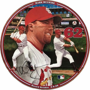 May include: A round, red, white, and blue baseball commemorative plate featuring a baseball player in a red and white uniform swinging a bat. The plate has the text "Mark McGwire", "62", "Record Breaker 9-8-98", and a signature.