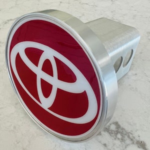 May include: A silver hitch cover with a red and white Toyota logo. The logo is a stylized circle with a white oval inside.