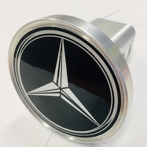 May include: A silver hitch cover with a black circle and a white Mercedes-Benz logo.