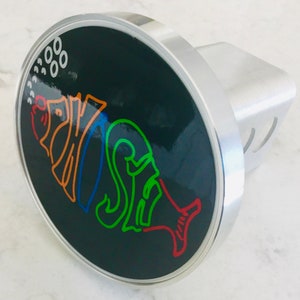 May include: A black and silver hitch cover with a colorful fish design. The fish is outlined in red, orange, green, and blue. The fish is surrounded by white dots.