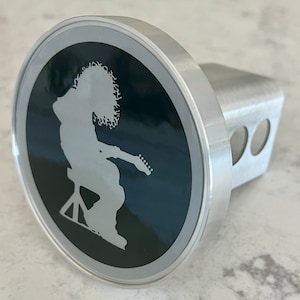 May include: A silver hitch cover with a black circle featuring a white silhouette of a person playing a guitar.