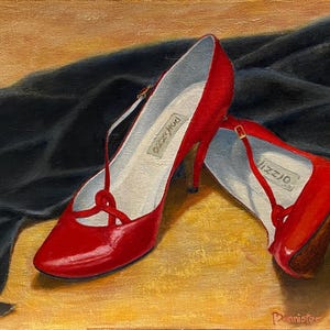 May include: A pair of red high-heeled shoes with a strap and buckle detail, resting on a golden surface next to a black fabric. The shoes have the brand name "Lizzio" printed on the insole.