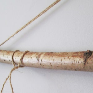 May include: A natural wood branch with a rough, brown bark texture is tied with twine to create a hanging display.