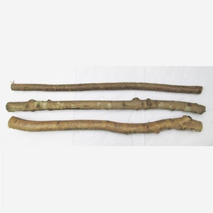 May include: Three brown wooden sticks of varying lengths and thicknesses. The sticks are lying on a white surface.